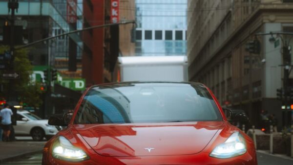 Red Tesla Model 3 car on an urban street with skyscrapers and cityscape view.