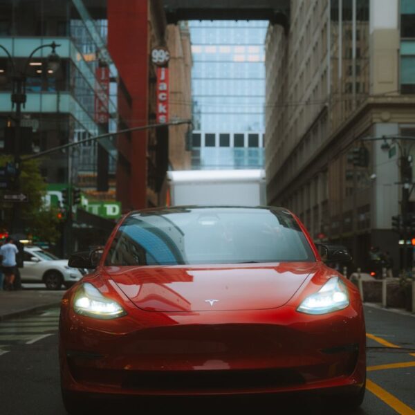Red Tesla Model 3 car on an urban street with skyscrapers and cityscape view.