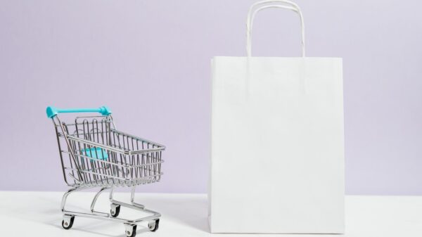Minimalist image of a white shopping bag and mini cart on a soft pastel background.
