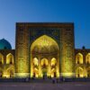 A stunning view of the Tilya-Kori Madrasah in Uzbekistan illuminated against a twilight sky, showcasing intricate architecture.