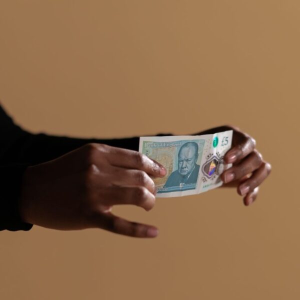 Hands holding a five-pound banknote, highlighting concept of cash and economy on a neutral backdrop.