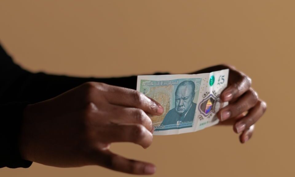Hands holding a five-pound banknote, highlighting concept of cash and economy on a neutral backdrop.