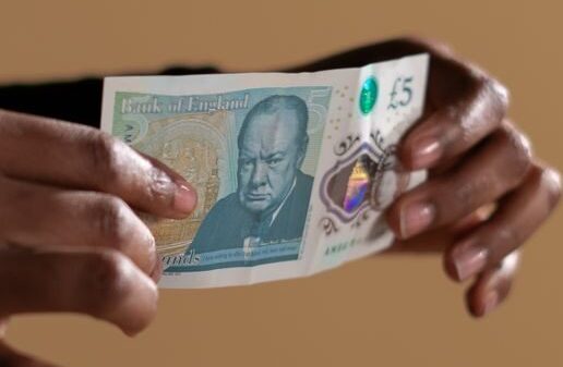 Hands holding a five-pound banknote, highlighting concept of cash and economy on a neutral backdrop.