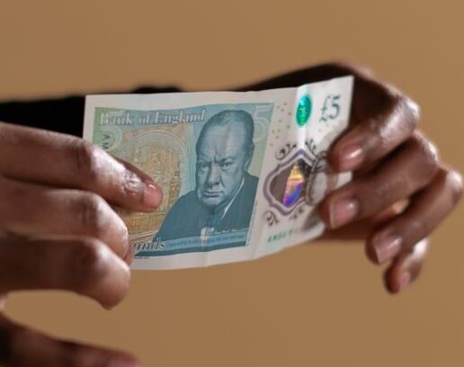 Hands holding a five-pound banknote, highlighting concept of cash and economy on a neutral backdrop.