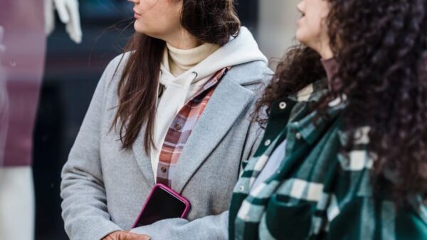 Pensive women friends in casual clothes standing with shopping bags near shop on street in daytime