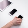 Overhead view of smartphones and a tablet on a white table with a hand reaching out.