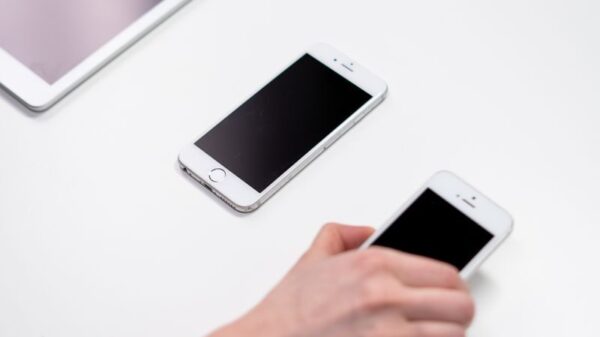 Overhead view of smartphones and a tablet on a white table with a hand reaching out.