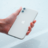 Close-up of a hand holding a white smartphone against a water droplet background.
