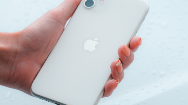 Close-up of a hand holding a white smartphone against a water droplet background.
