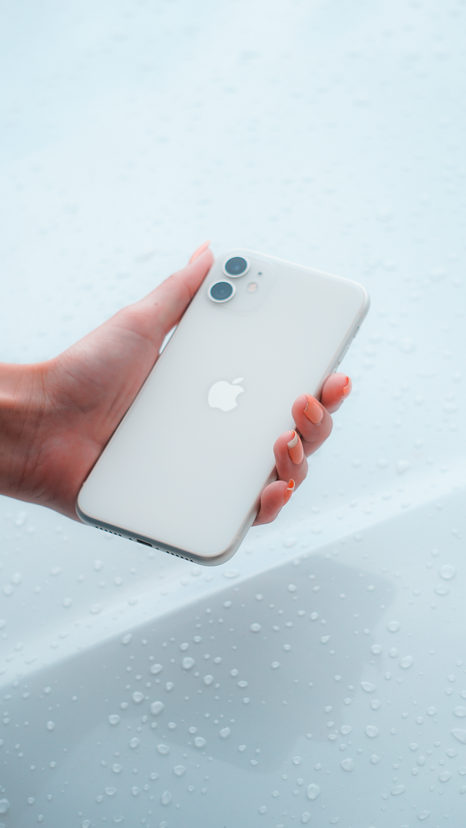 Close-up of a hand holding a white smartphone against a water droplet background.
