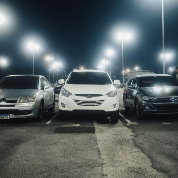 Night scene in a well-lit parking lot featuring various parked cars and street lamps.