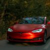 Sleek red electric car driving through a scenic forest road on an autumn day.