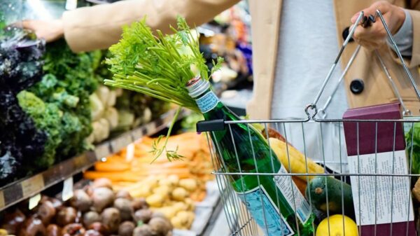 Woman selecting fresh produce in a supermarket with a basket full of groceries.
