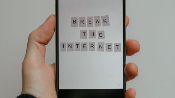 Close-up of a hand holding a smartphone displaying 'Break the Internet' on a gray background.