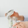 Close-up of hands placing money into a jar, symbolizing savings and financial planning.