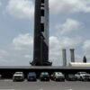 Tall rocket at launch pad with parked cars below under a cloudy blue sky