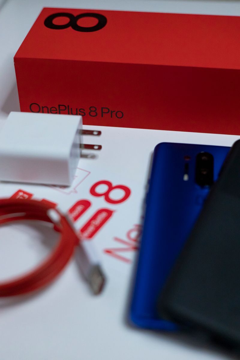 Flat lay of OnePlus 8 Pro unboxing with smartphone and accessories on white background.
