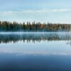 A tranquil Finnish lake reflects the forest and morning mist at sunrise.