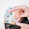 Close-up of a hand holding euro banknotes of different denominations, taken from a black wallet.