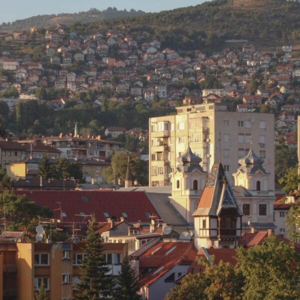 A picturesque view of Sarajevo cityscape with iconic buildings and surrounding hills at sunset.