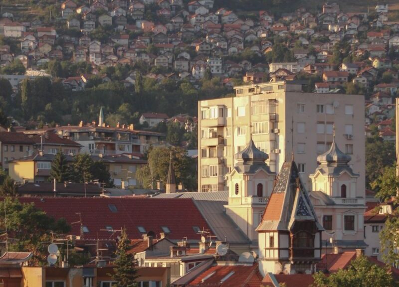 A picturesque view of Sarajevo cityscape with iconic buildings and surrounding hills at sunset.