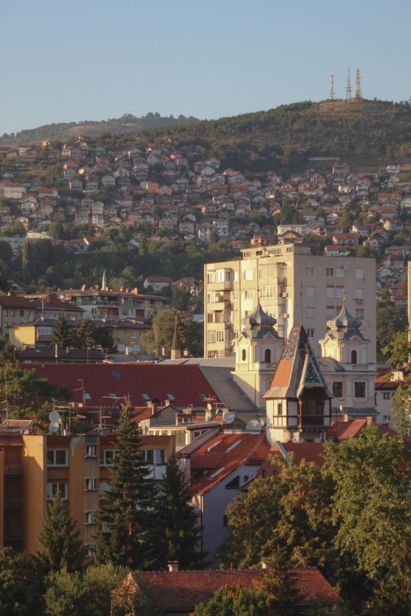 A picturesque view of Sarajevo cityscape with iconic buildings and surrounding hills at sunset.